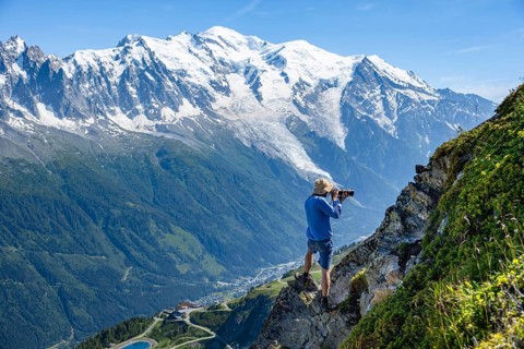 Photographer with zoom lens in mountain landscape, in front of glaciated mountain peak of Mont