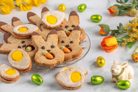 Bunny biscuits and egg biscuits decorated with icing next to Easter eggs and spring flowers