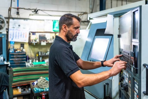 Mature man working on control panel of a lathe in cnc factory
