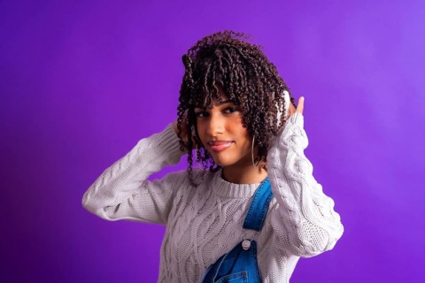 Young woman enjoying music with wireless headphones, wearing a white sweater and denim overalls,
