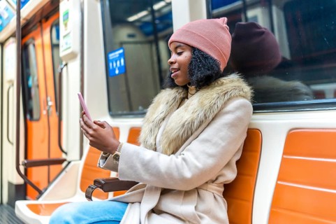 Stylish young woman commuting on a subway train, using her smartphone to browse social media and