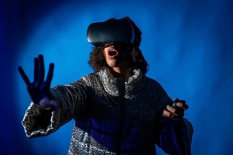 Excited young woman wearing vr headset and using controllers is experiencing metaverse on blue