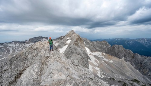 Mountaineer with helmet on a narrow rocky ridge, crossing the Jubiläumsgrat, behind the summit of