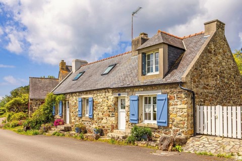 Idyllic old stone cottage by a road in the French countryside with flower pots by the wall on a