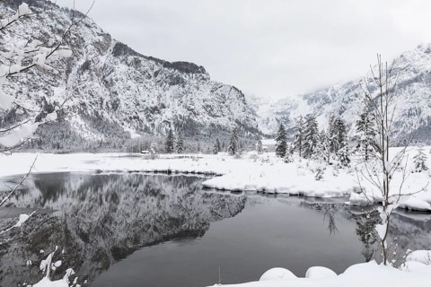 Snow covered Lake Almsee which is partly frozen and snow covered. Snow on the trees and mountains