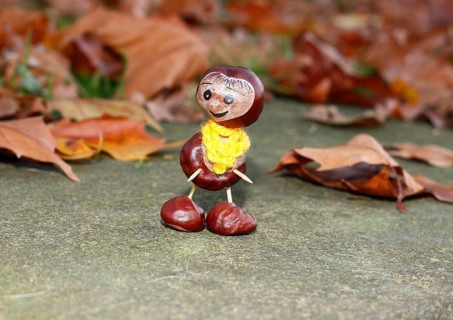 Funny chestnut figure with yellow scarf on a wall in autumn leaves, North Rhine-Westphalia,