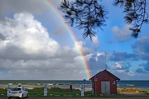 Beach landscape with rainbow and clouds over the sea and scattered green trees, car park, Tönsberg,