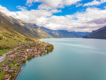 Village on the shore of a large lake, surrounded by mountains and clouds, panoramic style, Lake