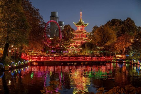 Illuminated pagoda, colourful lighting, roller coaster, trees, cityscape at night with modern