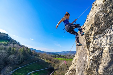 Female climber ascending a rock face, enjoying a sunny day and the beautiful view of the valley