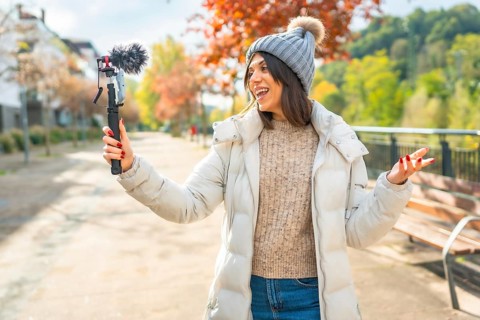 Caucasian young beauty female vlogger wearing warm winter clothes recording video in the city park