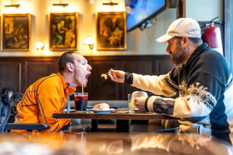Caregiver tenderly feeds a disabled man in a restaurant, highlighting the importance of support,