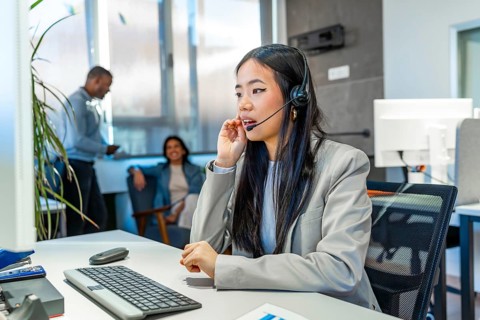 Young asian operator talking with headset and working on computer in a coworking office, with