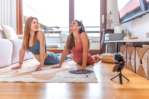 Two women recording an online yoga class from home, performing the cobra pose on a rug in the