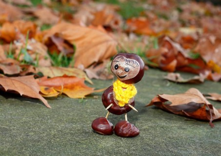 Funny chestnut figure with yellow scarf on a wall in autumn leaves, North Rhine-Westphalia,
