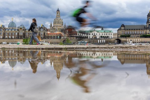 The Dresden silhouette with a cyclist and dark clouds behind the Church of Our Lady is reflected in