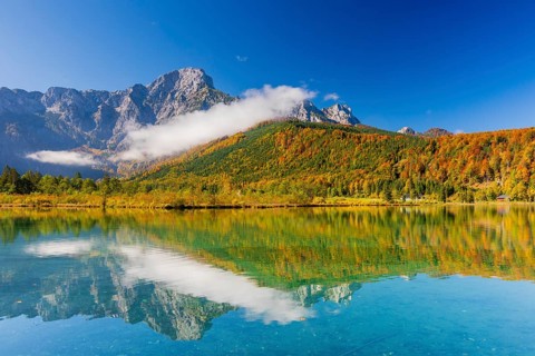 Lake Almsee in autumn with a forest reflected in the lake. A slowly dissipating fog moves over the