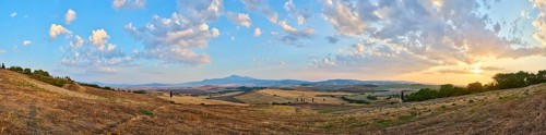 Typical Tuscan landscape in Val d'Orcia with hills, trees, fields, cypresses and farm road in