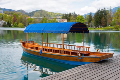 A single wooden boat with a blue roof lies on a platform in a calm lake, Lake Bled, Lake Veldes,