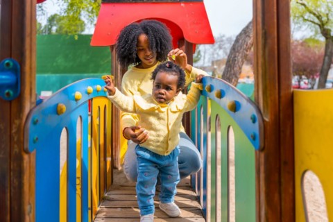 Frontal view of a young african mother and baby girl playing on playground
