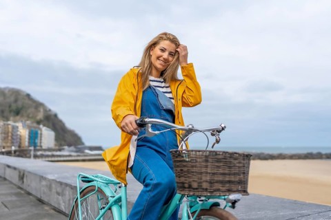 Young woman riding a bicycle along a beachfront promenade, enjoying the fresh air and coastal views