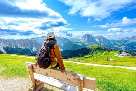 Hiker resting on a wooden bench admiring the beautiful mountain landscape of seceda in the italian