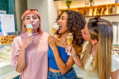 Happy diverse adult childish woman licking ice cream in store