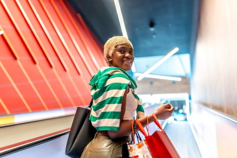 African woman using mechanical escalator in a shopping mall and turning to smile at camera