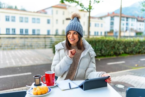 Creative caucasian beauty woman with warm clothes using digital tablet while drinking tea sitting