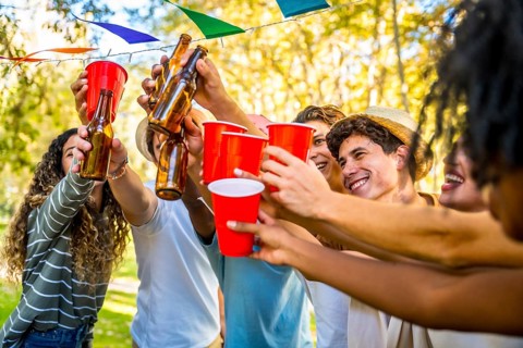 Multi-ethnic friends toasting with glasses and beer celebrating party together in a park