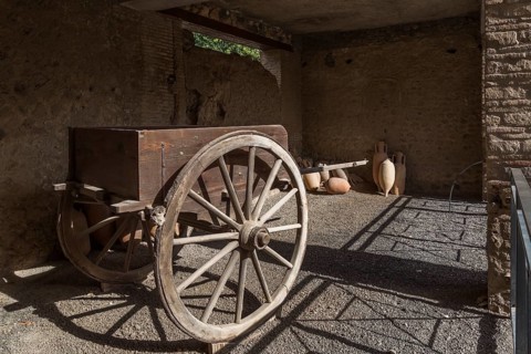 Old wooden cart and ceramic jugs on display inside an unenclosed building at the ancient ruins of