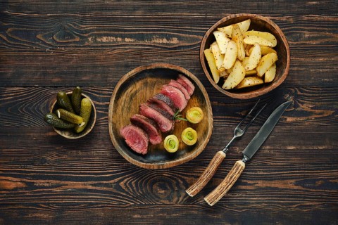 A beautifully arranged dinner features thinly sliced meat alongside roasted potatoes and pickles.