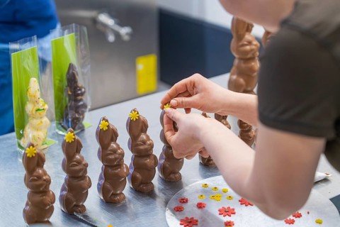 Person decorating several chocolate bunnies with flowers on a work table, Easter baking and