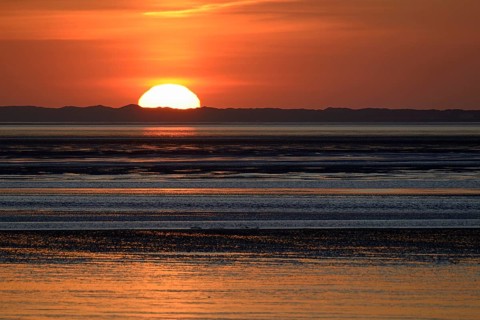 Sunset over the North Sea at low tide, the outline of the island of Juist on the horizon,
