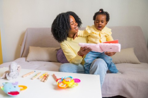 African mother and child smiling and reading a children's book sitting on the sofa
