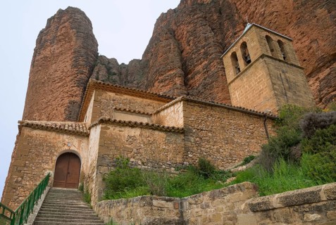 Historic church with bell tower and stone walls, situated at the foot of steep mountains, Las Peñas