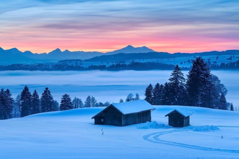 Sunset in the Allgäu in winter, view at sunset over the Forggensee with fog, in front two barns in