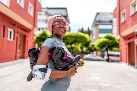 Side view of a modern african girl holding inline skates in the city