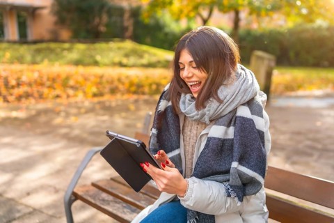 Rays of the sun illuminating a caucasian happy woman laughing while using digital tablet in a park