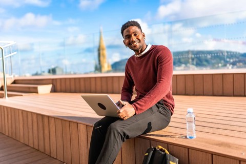 African man using laptop sitting on a terrace with views of a modern city