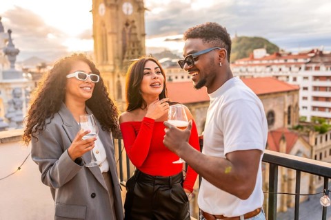 Multi-ethnic friends chatting and drinking wine in a rooftop during sunset with city views