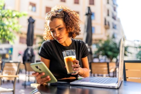 Young arab woman drinking iced coffee and using mobile phone while working with laptop in an