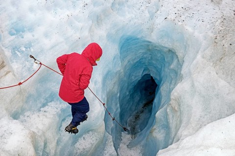 Mountaineer descending into a glacier Ice cave, Fox Glacier, Westland National Park, South Island,