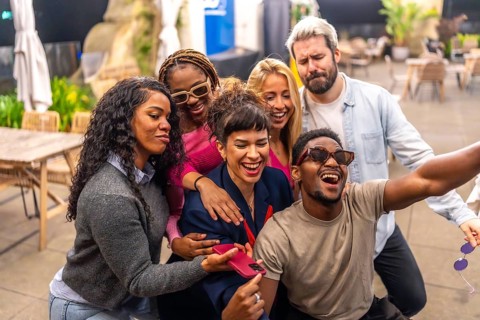 Happy group of multiracial friends taking selfie at night party in the terrace of a bar
