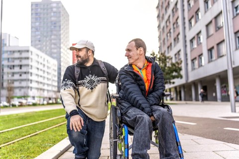 Caregiver assisting a disabled man in a wheelchair, enjoying a city stroll while engaging in