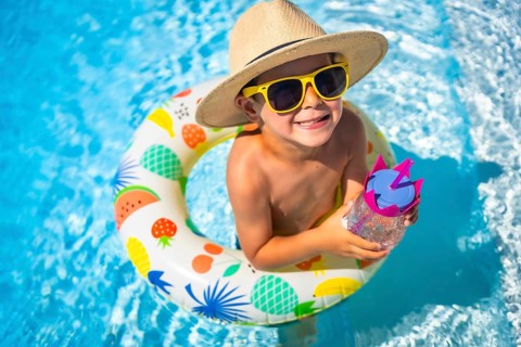 Top view close-up of a funny caucasian boy inside a pool drinking water into a rubber ring colorful