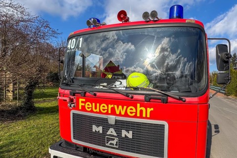 Front of red fire engine MAN truck with yellow lettering fire brigade above siren megaphone blue