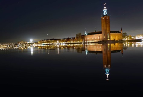 Illuminated building by a calm body of water at night with reflecting water and dark sky, capital
