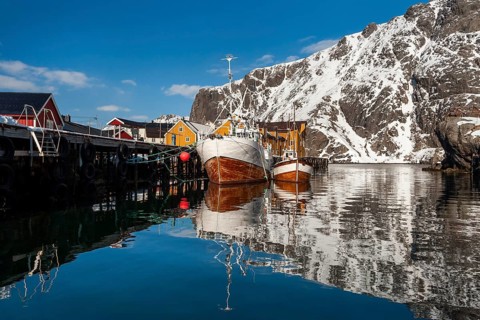 Fishing boats, fishing village with yellow houses in front of snowy mountains, Nusfjord,