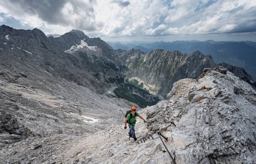 Mountaineer with helmet climbing on rock, on a narrow rocky ridge, view of Zugspitze and Höllental